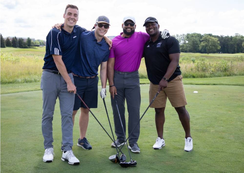 Four alumni showing off their golf clubs